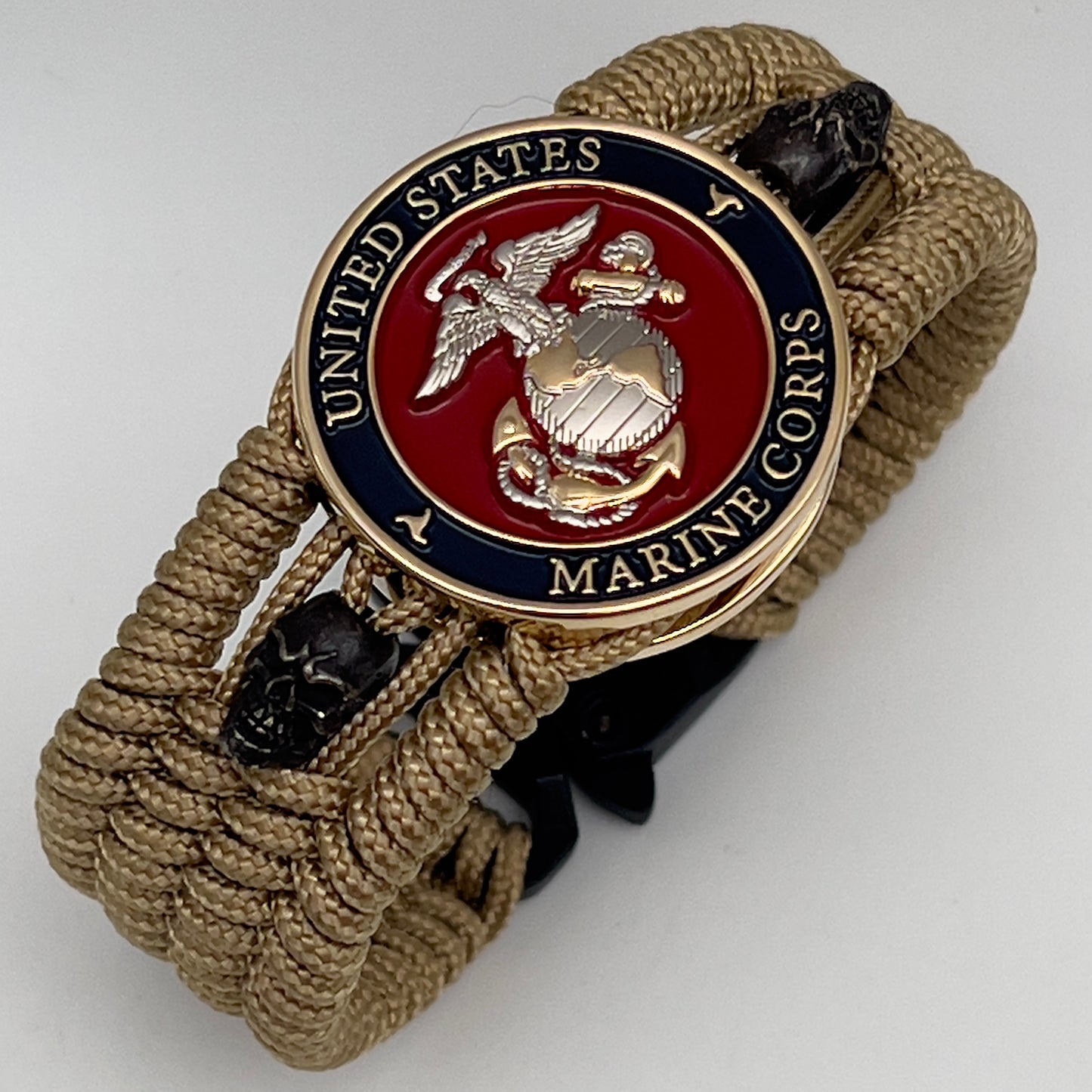 Thin, medium width, flexible and comfortable braided United States Marine Corps bracelet featuring a 24K gold and silver plated USMC officer Eagle Globe and Anchor medallion, two black micro skulls, a black Cobra style tactical buckle and woven with gold type-1 paracord.
