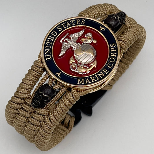 Thin, medium width, flexible and comfortable braided United States Marine Corps bracelet featuring a 24K gold and silver plated USMC officer Eagle Globe and Anchor medallion, two black micro skulls, a black Cobra style tactical buckle and woven with gold type-1 paracord.