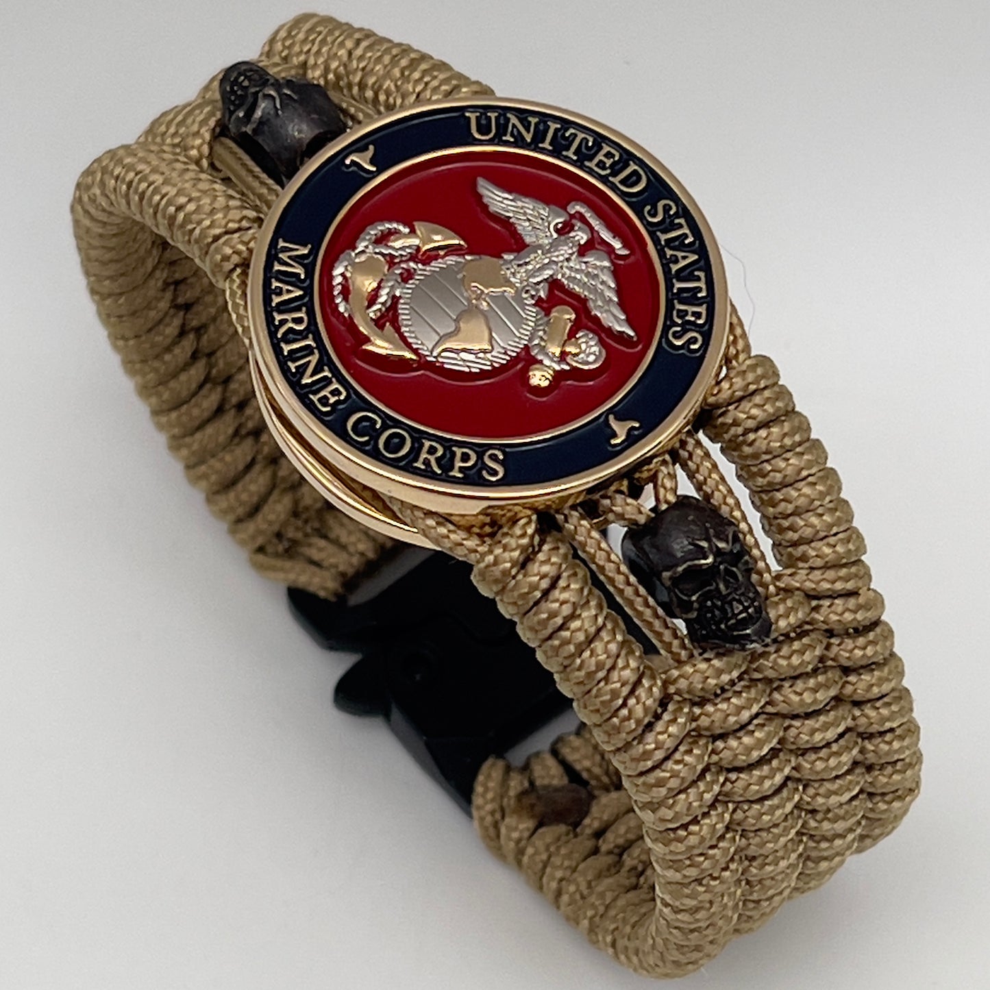 Thin, medium width, flexible and comfortable braided United States Marine Corps bracelet featuring a 24K gold and silver plated USMC officer Eagle Globe and Anchor medallion, two black micro skulls, a black Cobra style tactical buckle and woven with gold type-1 paracord.