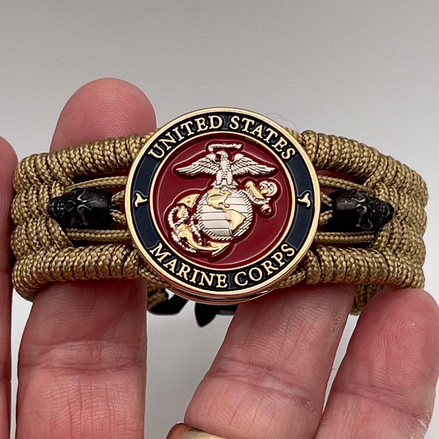 Thin, medium width, flexible and comfortable braided United States Marine Corps bracelet featuring a 24K gold and silver plated USMC officer Eagle Globe and Anchor medallion, two black micro skulls, a black Cobra style tactical buckle and woven with gold type-1 paracord.