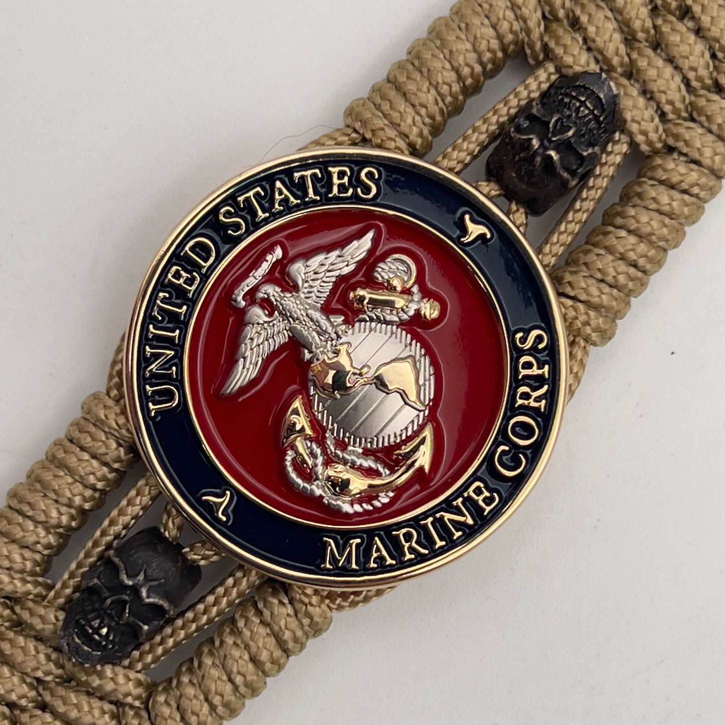 Thin, medium width, flexible and comfortable braided United States Marine Corps bracelet featuring a 24K gold and silver plated USMC officer Eagle Globe and Anchor medallion, two black micro skulls, a black Cobra style tactical buckle and woven with gold type-1 paracord.