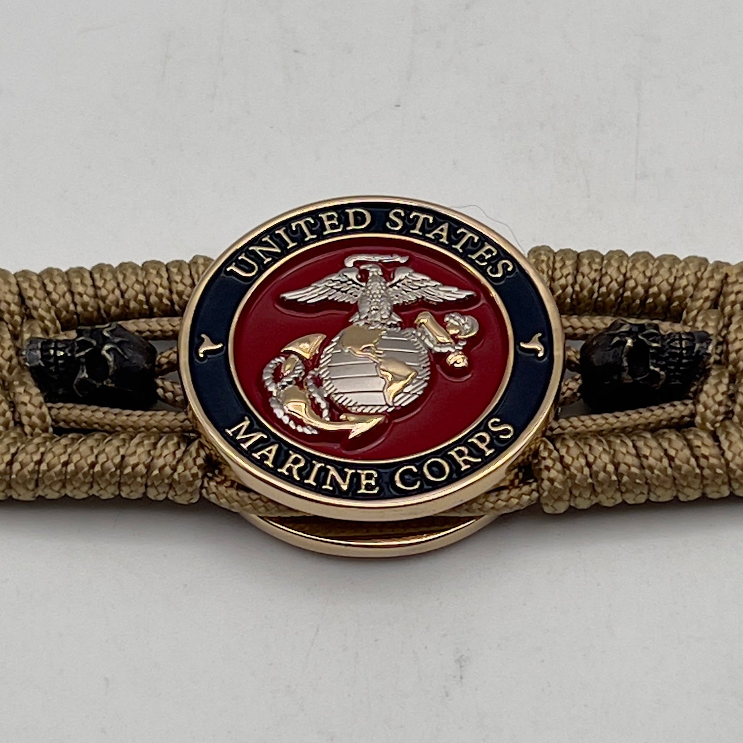 Thin, medium width, flexible and comfortable braided United States Marine Corps bracelet featuring a 24K gold and silver plated USMC officer Eagle Globe and Anchor medallion, two black micro skulls, a black Cobra style tactical buckle and woven with gold type-1 paracord.