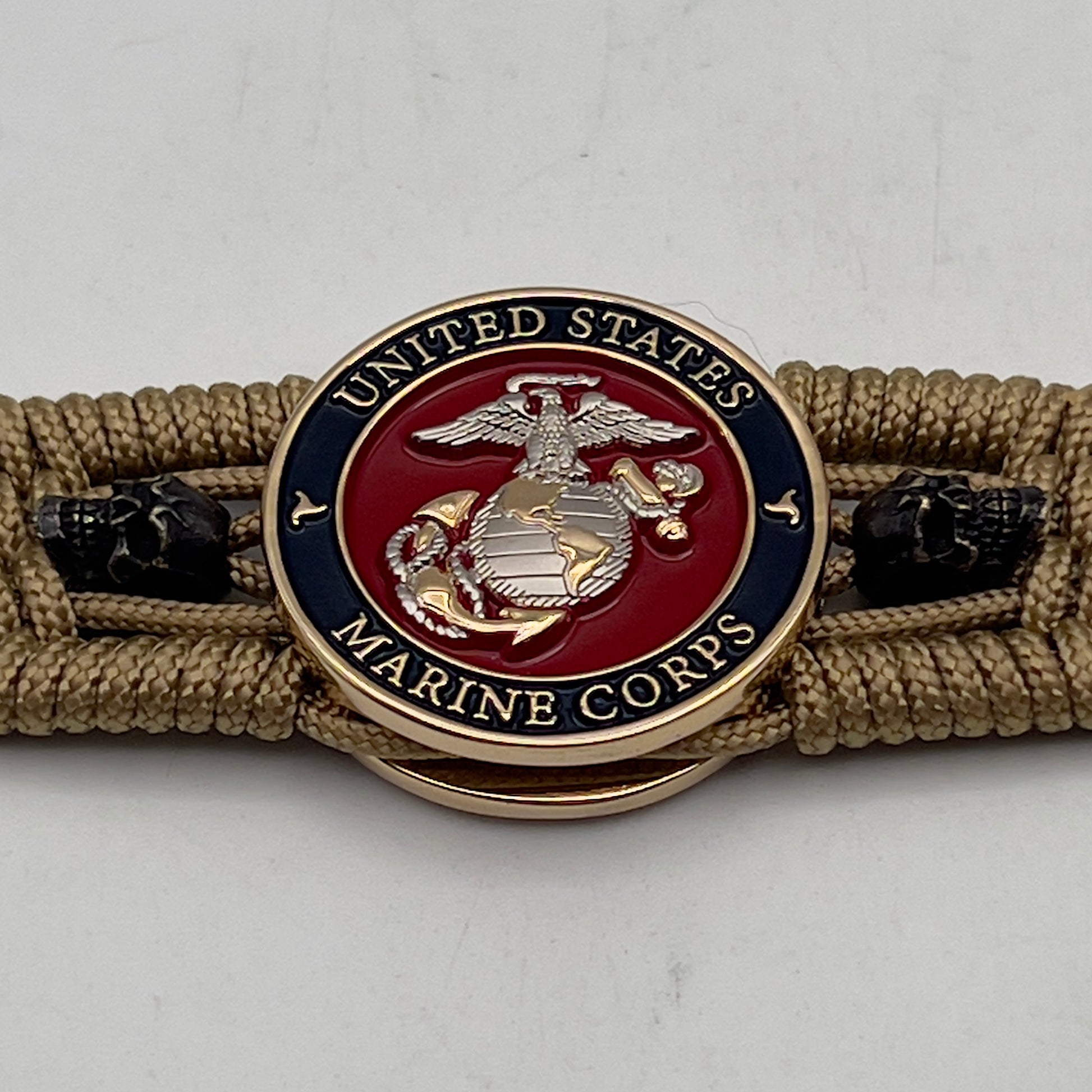 Thin, medium width, flexible and comfortable braided United States Marine Corps bracelet featuring a 24K gold and silver plated USMC officer Eagle Globe and Anchor medallion, two black micro skulls, a black Cobra style tactical buckle and woven with gold type-1 paracord.