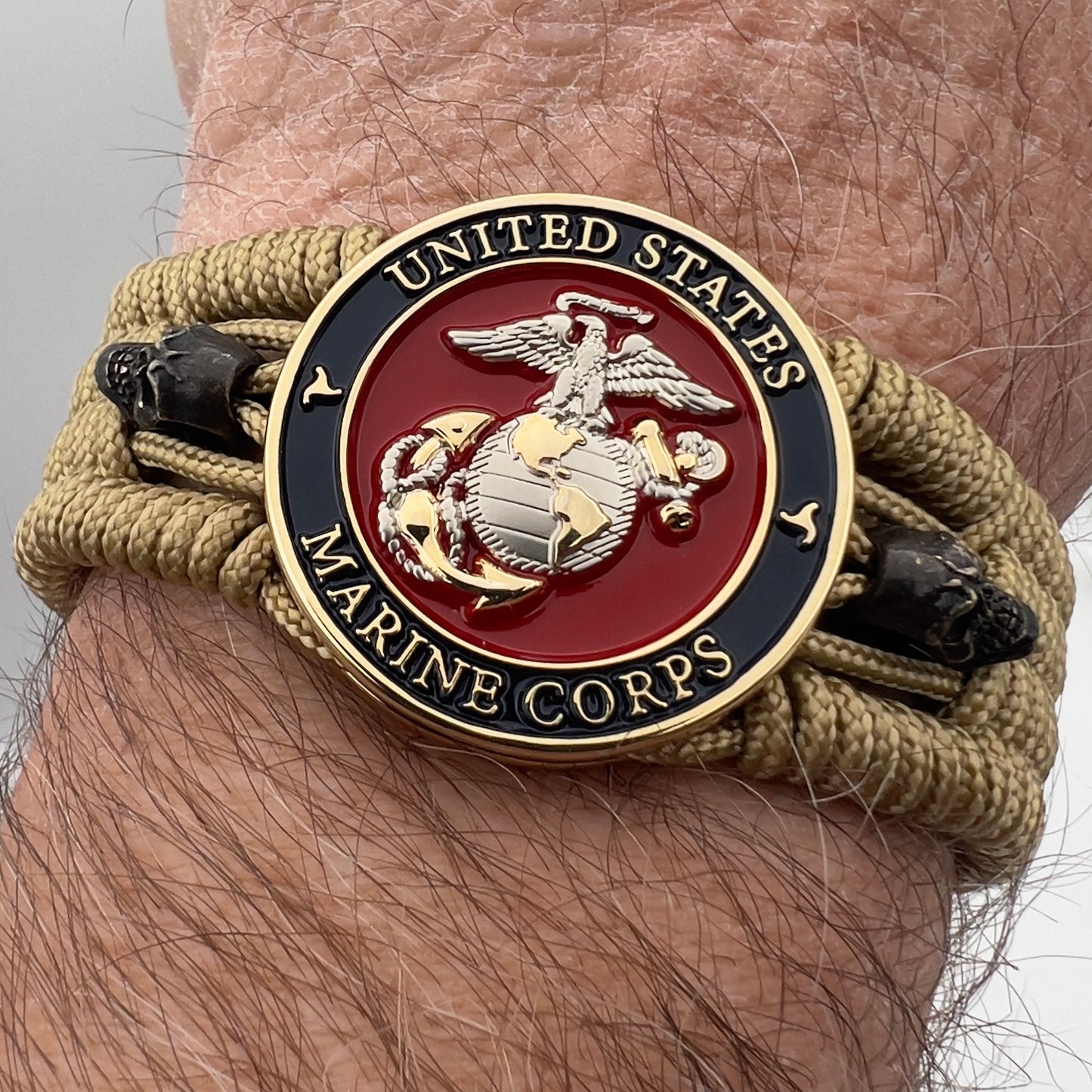 Thin, medium width, flexible and comfortable braided United States Marine Corps bracelet featuring a 24K gold and silver plated USMC officer Eagle Globe and Anchor medallion, two black micro skulls, a black Cobra style tactical buckle and woven with gold type-1 paracord.