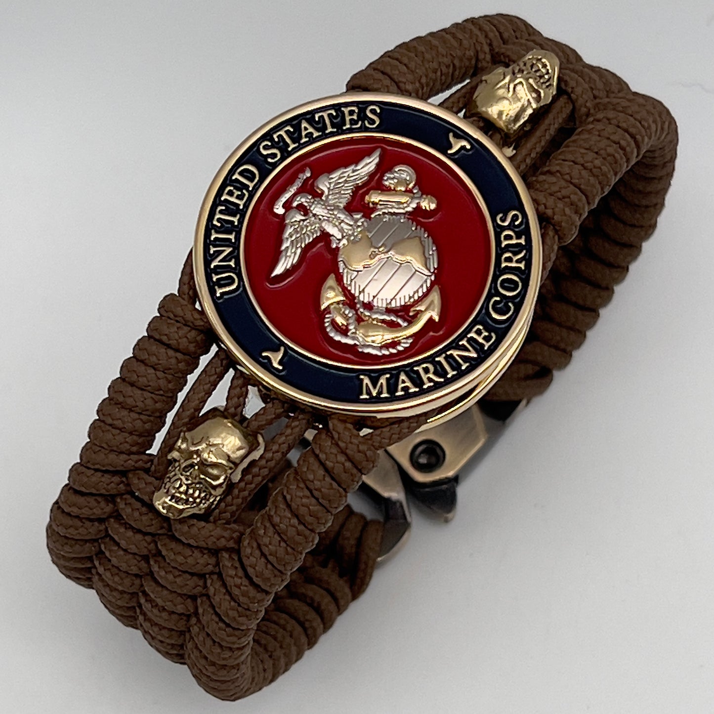 Thin, medium width, flexible and comfortable braided United States Marine Corps bracelet featuring a 24K gold and silver plated USMC officer Eagle Globe and Anchor medallion, two gold micro skulls, a gold Cobra style tactical buckle and woven with Coyote Brown type-1 paracord.