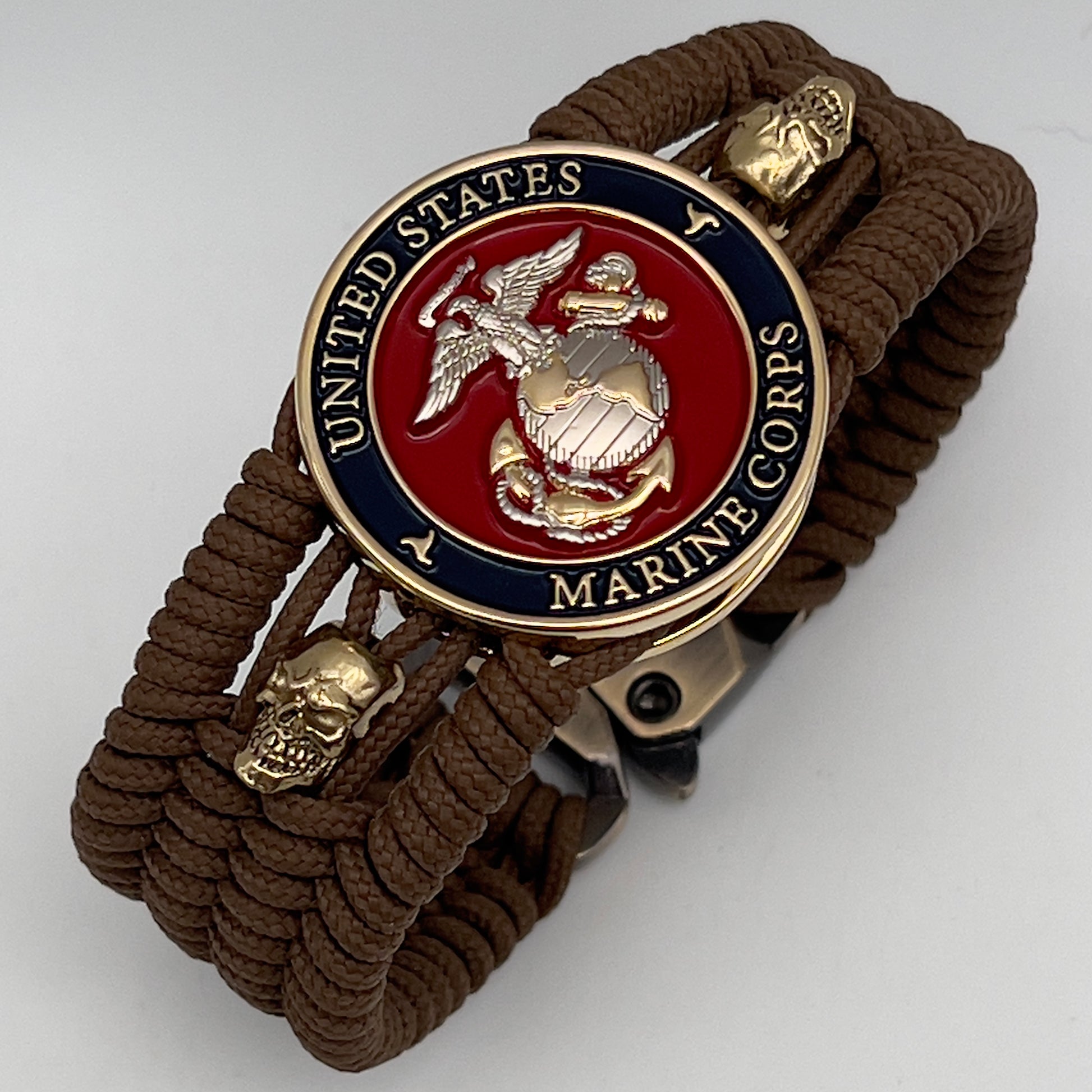 Thin, medium width, flexible and comfortable braided United States Marine Corps bracelet featuring a 24K gold and silver plated USMC officer Eagle Globe and Anchor medallion, two gold micro skulls, a gold Cobra style tactical buckle and woven with Coyote Brown type-1 paracord.