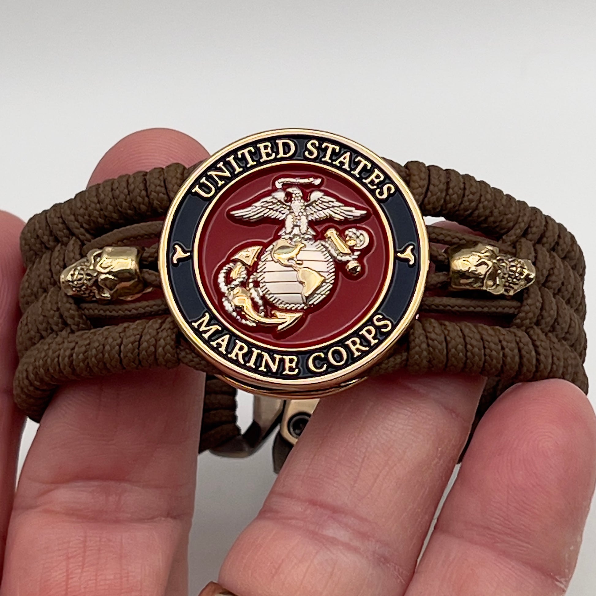 Thin, medium width, flexible and comfortable braided United States Marine Corps bracelet featuring a 24K gold and silver plated USMC officer Eagle Globe and Anchor medallion, two gold micro skulls, a gold Cobra style tactical buckle and woven with Coyote Brown type-1 paracord.