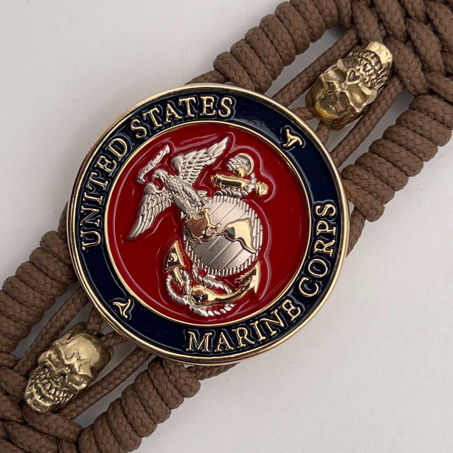 Thin, medium width, flexible and comfortable braided United States Marine Corps bracelet featuring a 24K gold and silver plated USMC officer Eagle Globe and Anchor medallion, two gold micro skulls, a gold Cobra style tactical buckle and woven with Coyote Brown type-1 paracord.