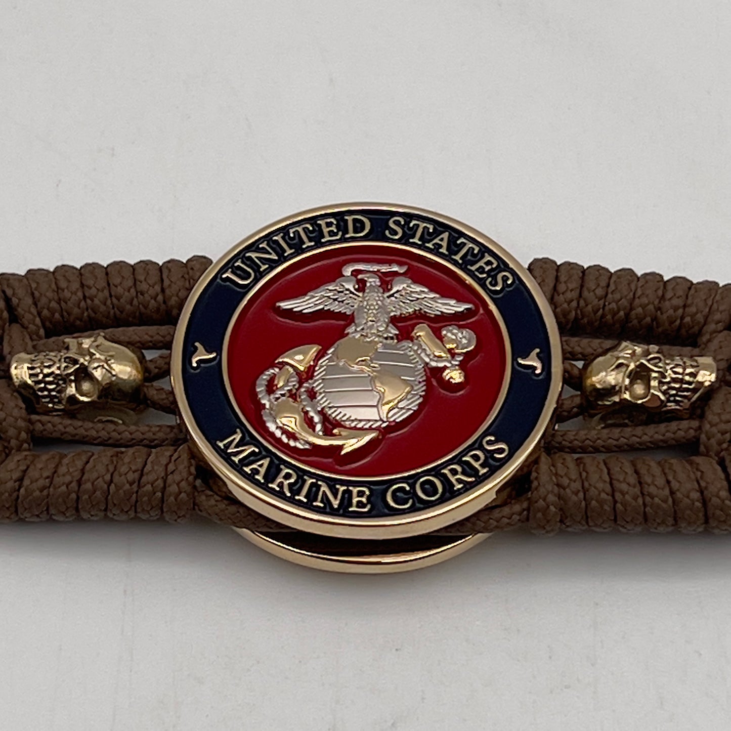 Thin, medium width, flexible and comfortable braided United States Marine Corps bracelet featuring a 24K gold and silver plated USMC officer Eagle Globe and Anchor medallion, two gold micro skulls, a gold Cobra style tactical buckle and woven with Coyote Brown type-1 paracord.