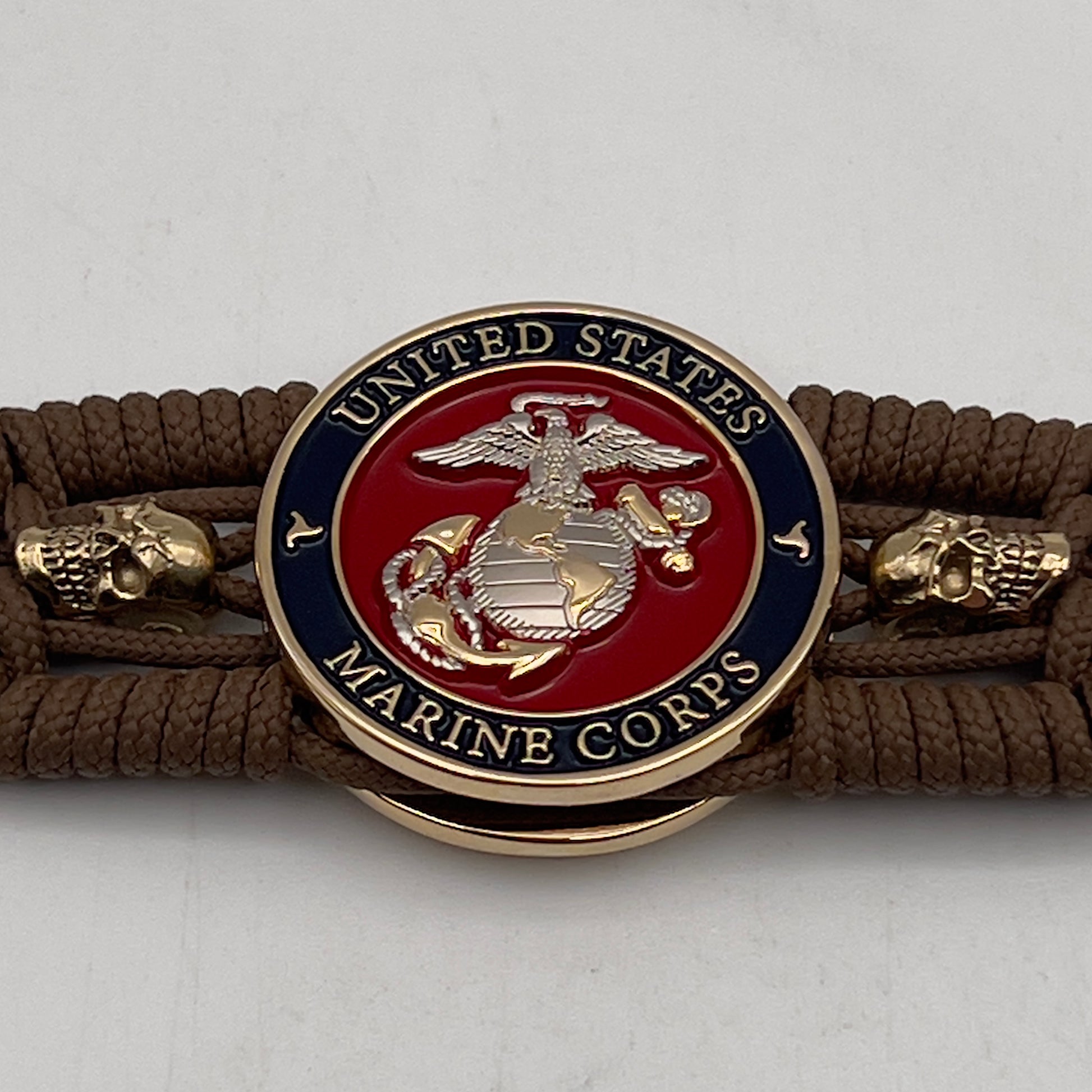 Thin, medium width, flexible and comfortable braided United States Marine Corps bracelet featuring a 24K gold and silver plated USMC officer Eagle Globe and Anchor medallion, two gold micro skulls, a gold Cobra style tactical buckle and woven with Coyote Brown type-1 paracord.