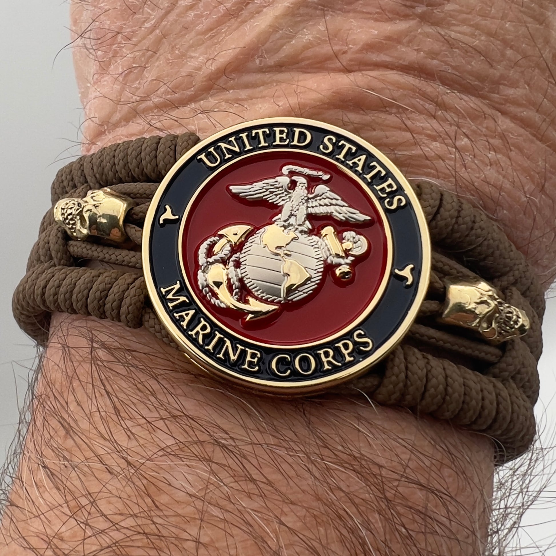 Thin, medium width, flexible and comfortable braided United States Marine Corps bracelet featuring a 24K gold and silver plated USMC officer Eagle Globe and Anchor medallion, two gold micro skulls, a gold Cobra style tactical buckle and woven with Coyote Brown type-1 paracord.