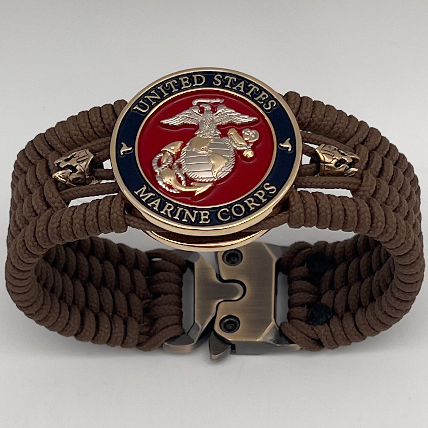 Thin, medium width, flexible and comfortable braided United States Marine Corps bracelet featuring a 24K gold and silver plated USMC officer Eagle Globe and Anchor medallion, two brass micro Spartan helmets, a gold Cobra style tactical buckle and woven with Coyote Brown type-1 paracord.