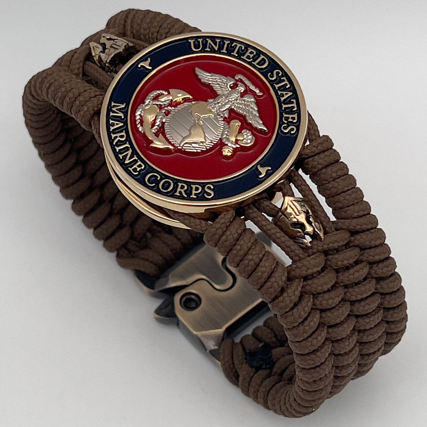 Thin, medium width, flexible and comfortable braided United States Marine Corps bracelet featuring a 24K gold and silver plated USMC officer Eagle Globe and Anchor medallion, two brass micro Spartan helmets, a gold Cobra style tactical buckle and woven with Coyote Brown type-1 paracord.