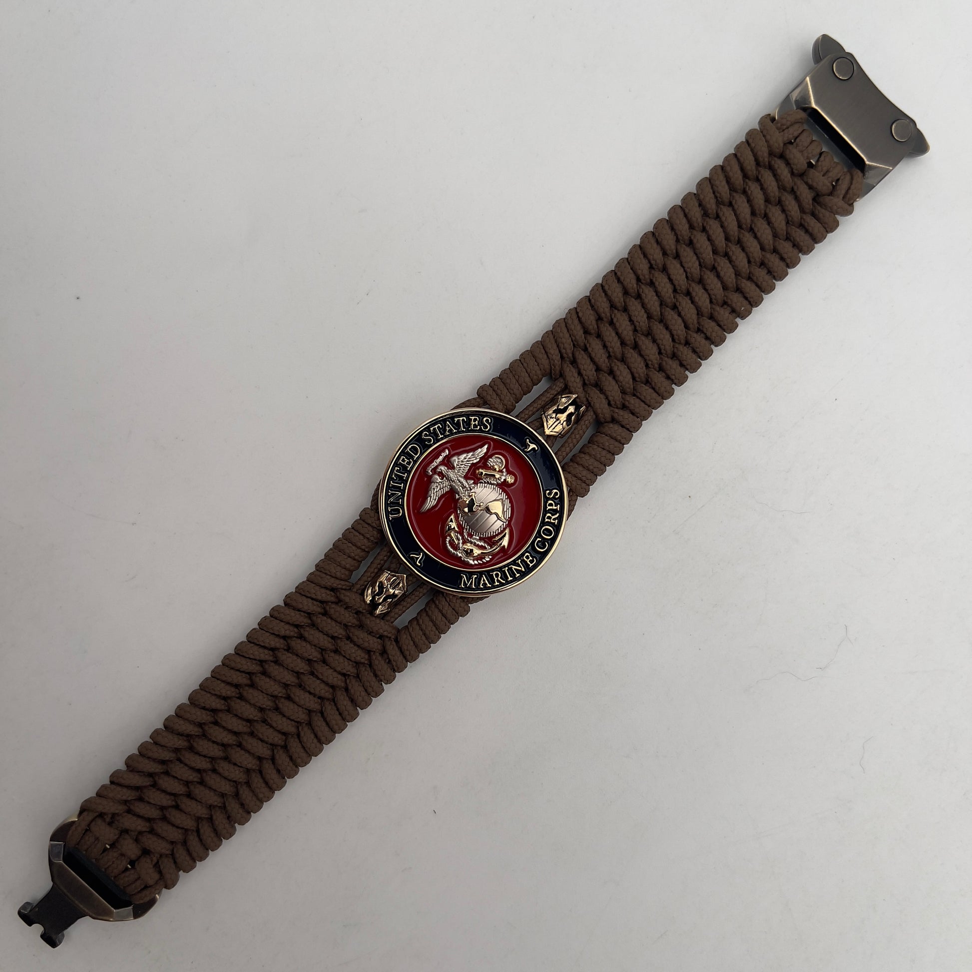 Thin, medium width, flexible and comfortable braided United States Marine Corps bracelet featuring a 24K gold and silver plated USMC officer Eagle Globe and Anchor medallion, two brass micro Spartan helmets, a gold Cobra style tactical buckle and woven with Coyote Brown type-1 paracord.