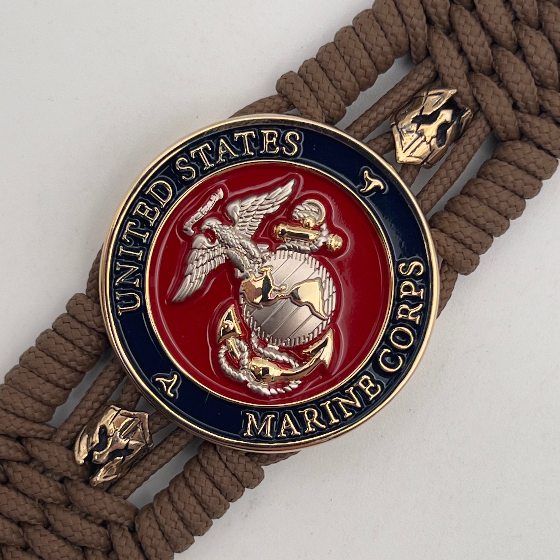Thin, medium width, flexible and comfortable braided United States Marine Corps bracelet featuring a 24K gold and silver plated USMC officer Eagle Globe and Anchor medallion, two brass micro Spartan helmets, a gold Cobra style tactical buckle and woven with Coyote Brown type-1 paracord.