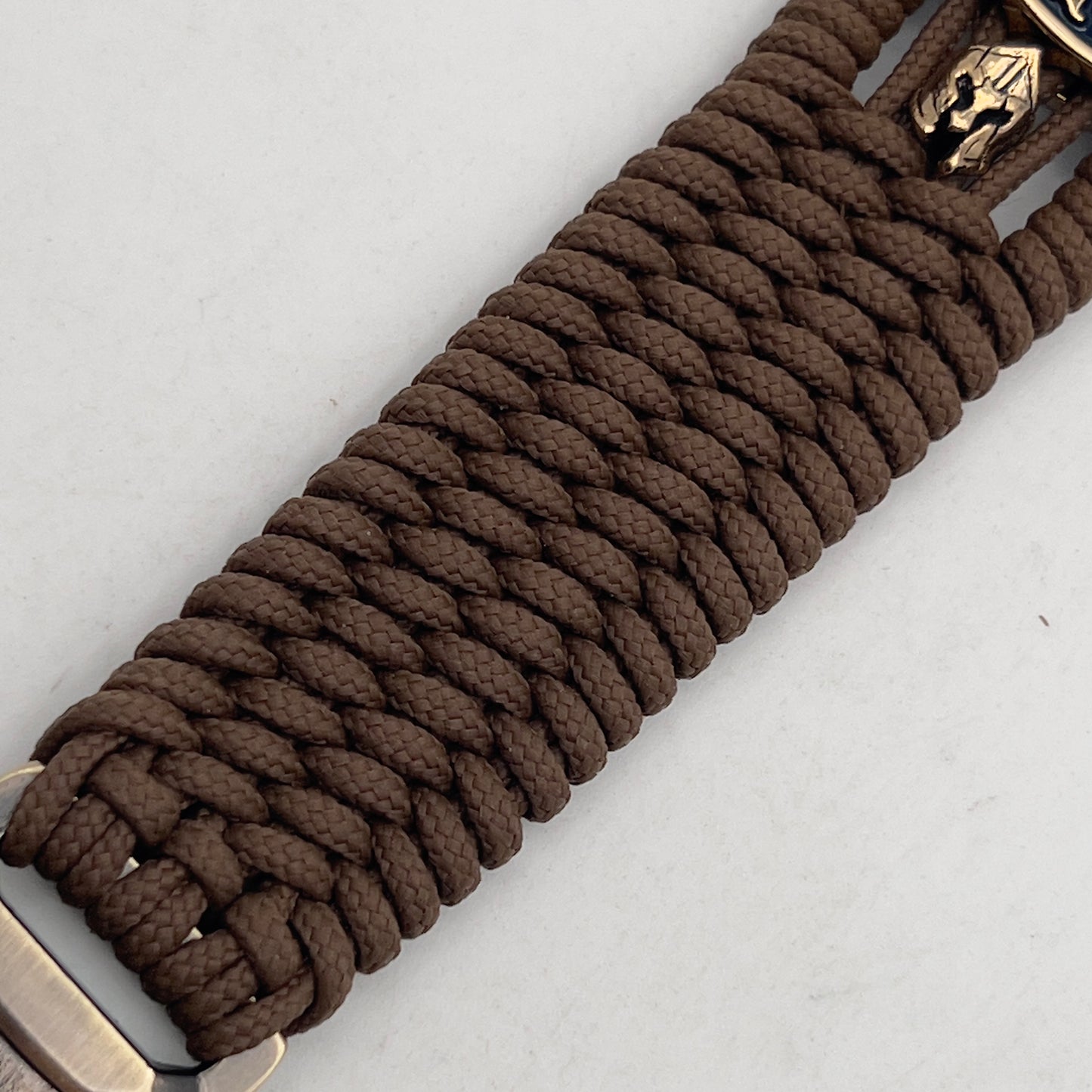 Thin, medium width, flexible and comfortable braided United States Marine Corps bracelet featuring a 24K gold and silver plated USMC officer Eagle Globe and Anchor medallion, two brass micro Spartan helmets, a gold Cobra style tactical buckle and woven with Coyote Brown type-1 paracord.