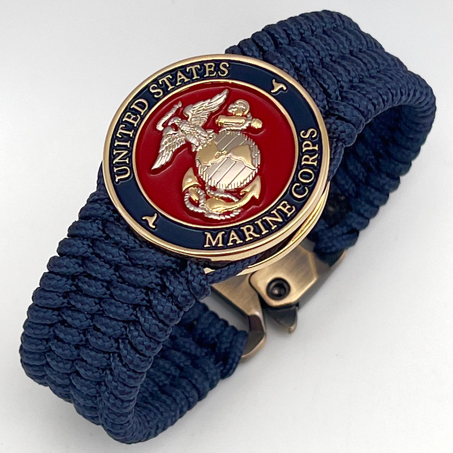 Thin, wide, flexible and comfortable braided United States Marine Corps bracelet featuring a 24K gold and silver plated USMC Eagle Globe and Anchor medallion, a gold Cobra style tactical buckle and woven with Navy blue type-1 paracord.