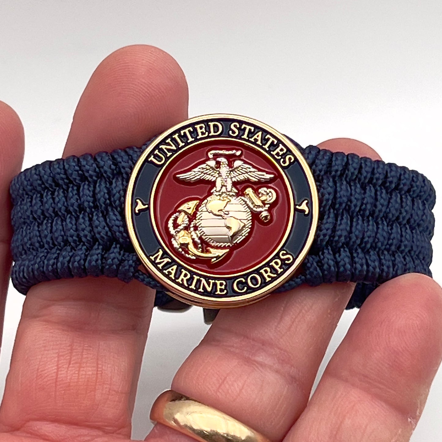 Thin, wide, flexible and comfortable braided United States Marine Corps bracelet featuring a 24K gold and silver plated USMC Eagle Globe and Anchor medallion, a gold Cobra style tactical buckle and woven with Navy blue type-1 paracord.