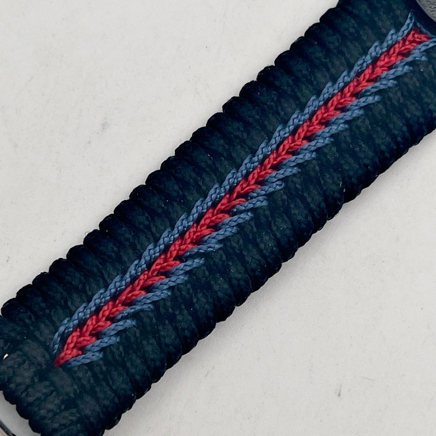 Thin, medium width, flexible and comfortable braided United States Marine Corps bracelet featuring a black USMC Eagle Globe and Anchor medallion, a black Cobra style tactical buckle and woven with black Type-1 paracord and stitched with red and blue nano cord.