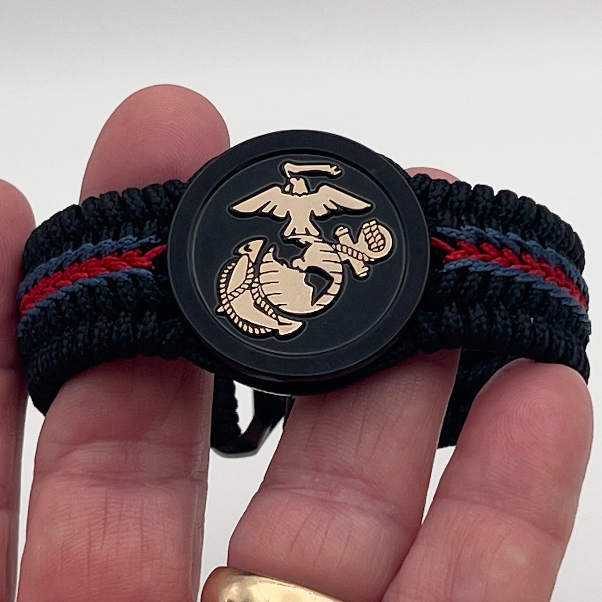 Thin, medium width, flexible and comfortable braided United States Marine Corps bracelet featuring a black USMC Eagle Globe and Anchor medallion, a black Cobra style tactical buckle and woven with black Type-1 paracord and blue and red nano cord.