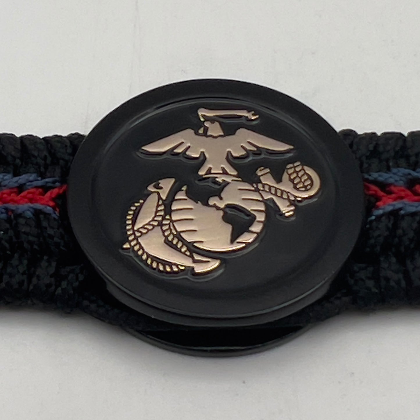 Thin, medium width, flexible and comfortable braided United States Marine Corps bracelet featuring a black USMC Eagle Globe and Anchor medallion, a black Cobra style tactical buckle and woven with black Type-1 paracord and blue and red nano cord.