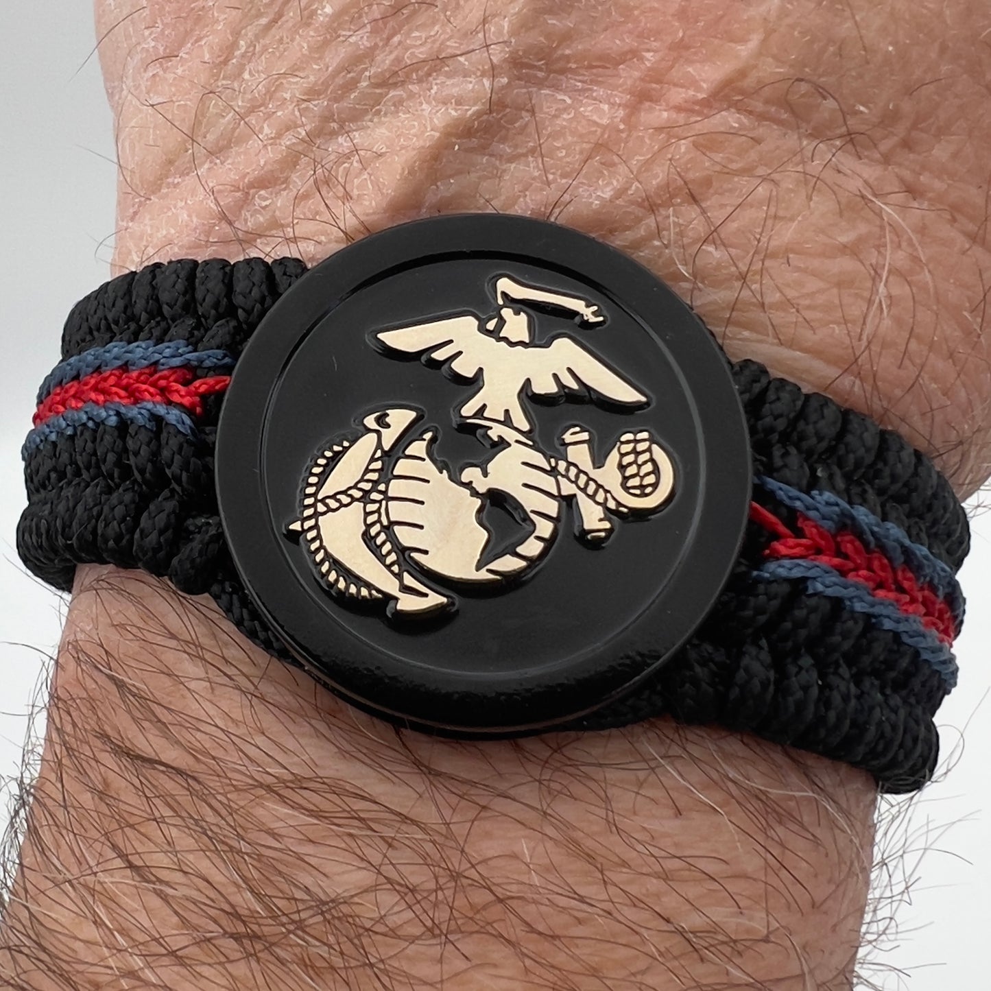 Thin, medium width, flexible and comfortable braided United States Marine Corps bracelet featuring a black USMC Eagle Globe and Anchor medallion, a black Cobra style tactical buckle and woven with black Type-1 paracord and blue and red nano cord.