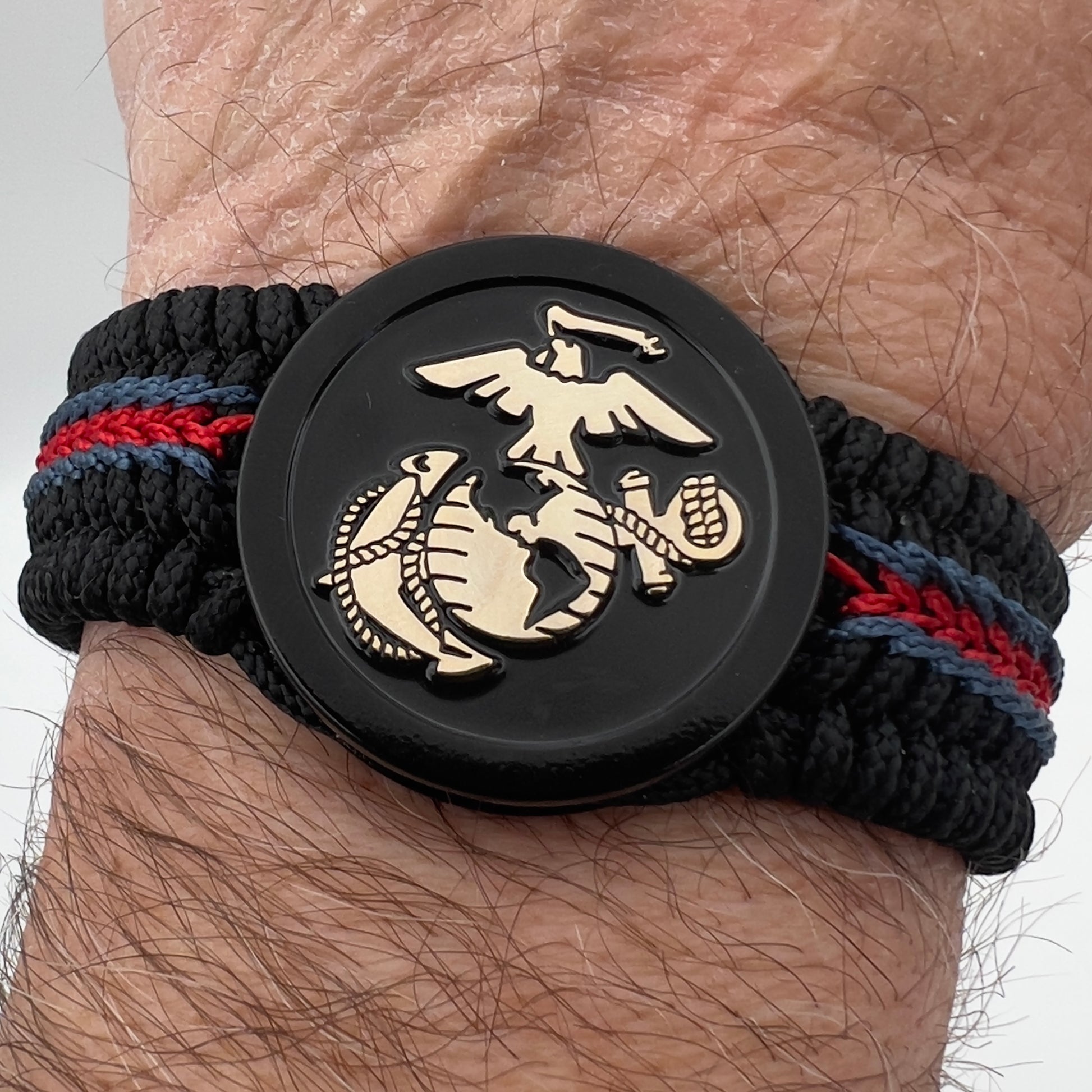 Thin, medium width, flexible and comfortable braided United States Marine Corps bracelet featuring a black USMC Eagle Globe and Anchor medallion, a black Cobra style tactical buckle and woven with black Type-1 paracord and blue and red nano cord.