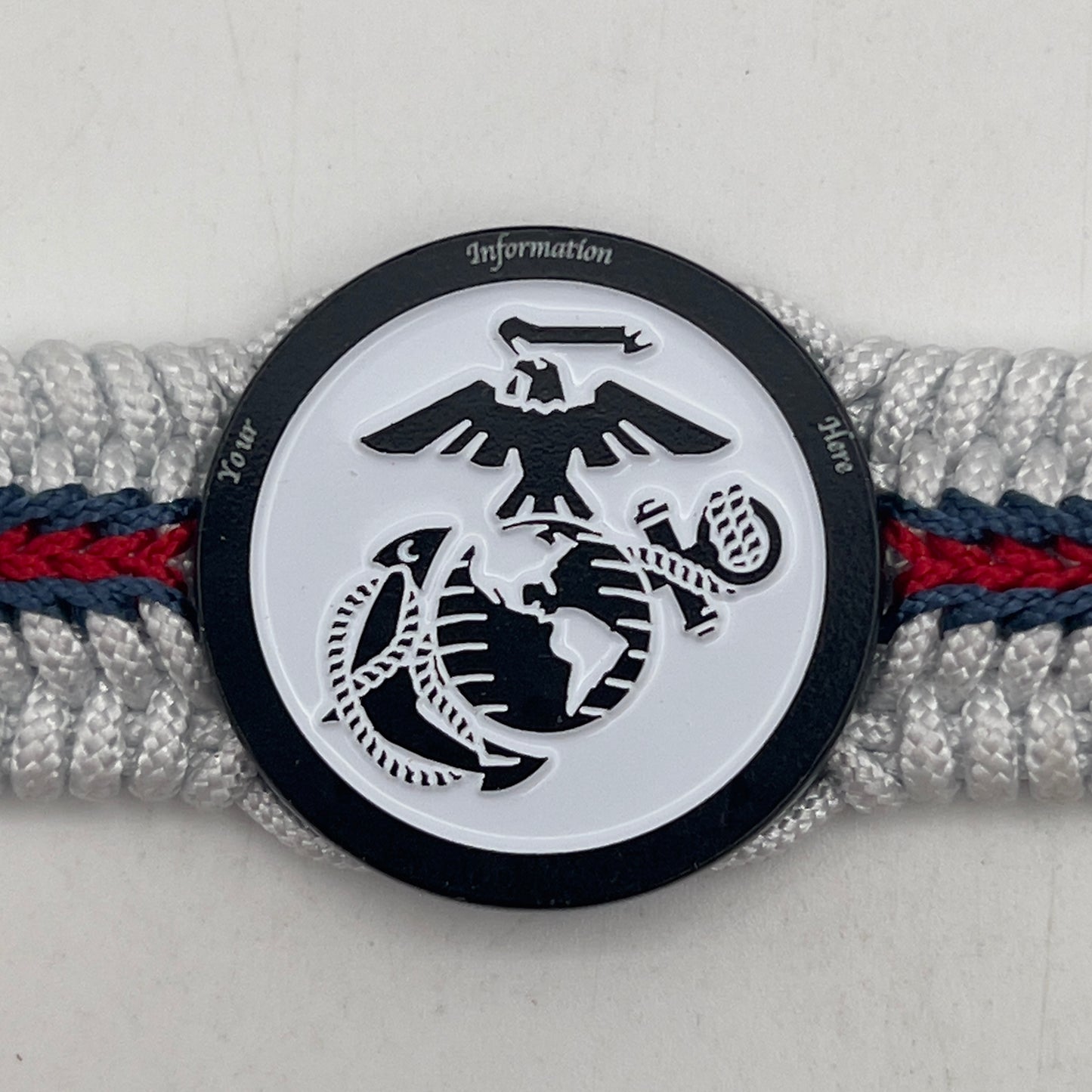 Thin, medium width, flexible and comfortable braided United States Marine Corps bracelet featuring a black USMC Eagle Globe and Anchor medallion, a black Cobra style tactical buckle and woven with white Type-1 paracord and stitched with red and blue nano cord.