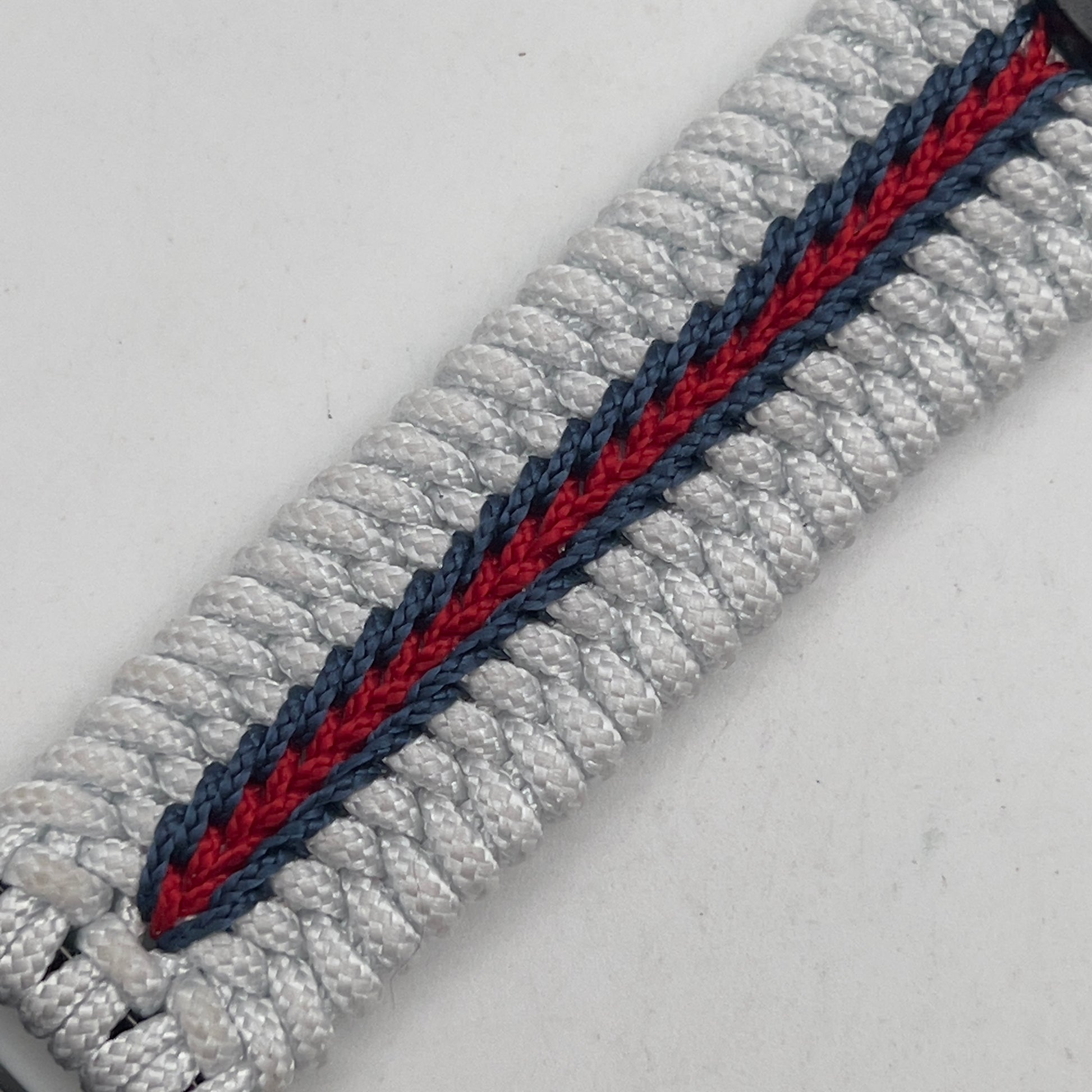 Thin, medium width, flexible and comfortable braided United States Marine Corps bracelet featuring a black USMC Eagle Globe and Anchor medallion, a black Cobra style tactical buckle and woven with white Type-1 paracord and stitched with red and blue nano cord.