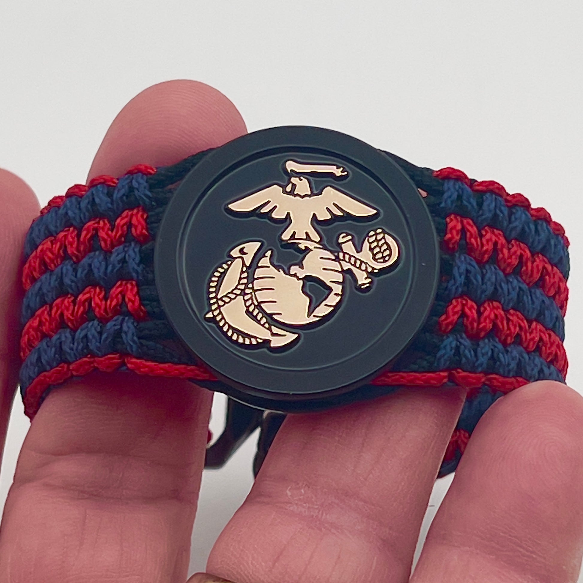 Thin, medium width, flexible and comfortable braided United States Marine Corps bracelet featuring a black USMC Eagle Globe and Anchor medallion, a black Cobra style tactical buckle and woven with black Type-1 paracord and blue and red nano cord.
