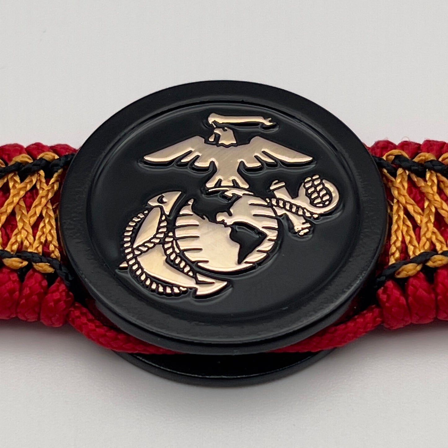 Thin, narrow, flexible and comfortable braided United States Marine Corps bracelet featuring the official US Marine Corps Eagle, Globe and Anchor medallion, a black Cobra style tactical buckle and woven with red Type-1 paracord and center stitched with black and goldenrod nano cord.