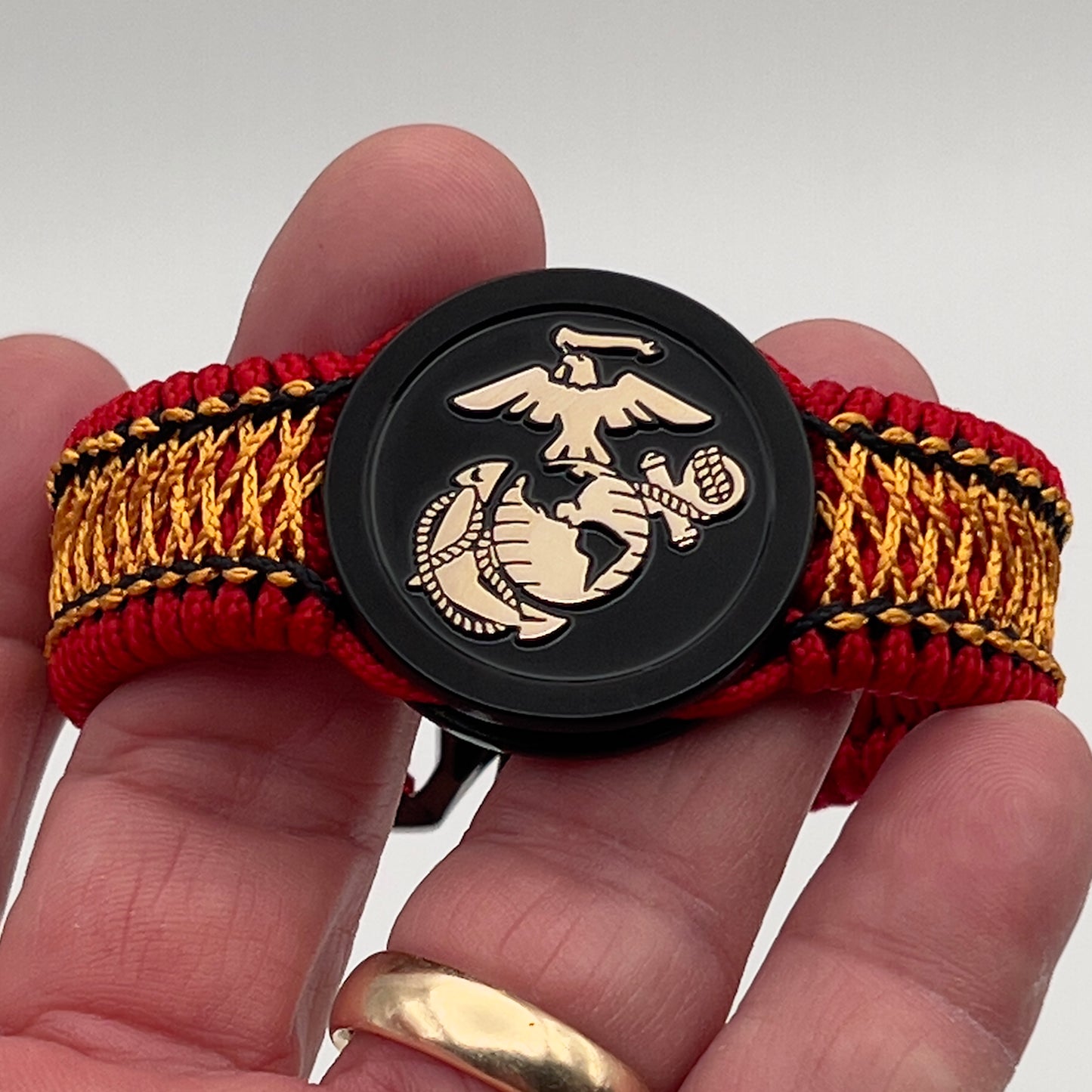 Thin, narrow, flexible and comfortable braided United States Marine Corps bracelet featuring the official US Marine Corps Eagle, Globe and Anchor medallion, a black Cobra style tactical buckle and woven with red Type-1 paracord and center stitched with black and goldenrod nano cord.