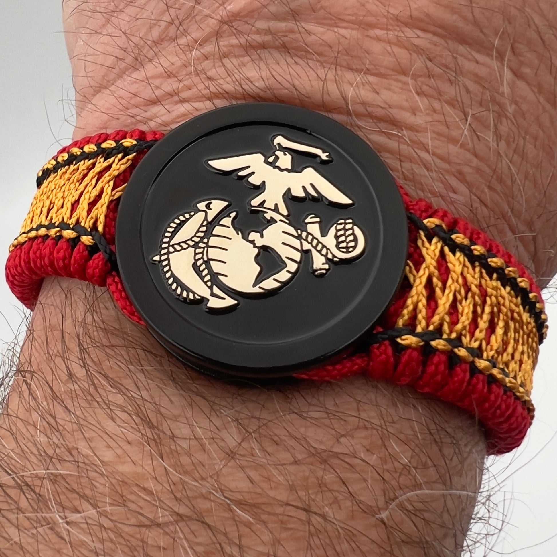 Thin, narrow, flexible and comfortable braided United States Marine Corps bracelet featuring the official US Marine Corps Eagle, Globe and Anchor medallion, a black Cobra style tactical buckle and woven with red Type-1 paracord and center stitched with black and goldenrod nano cord.