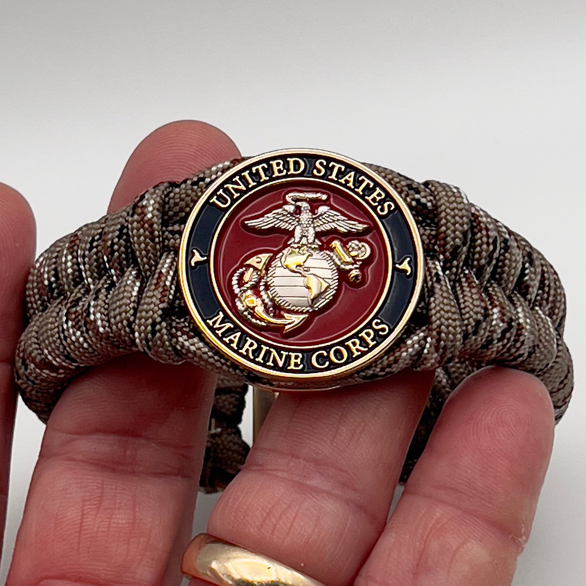 Thick and comfortable braided United States Marine Corps bracelet featuring a 24K gold and silver plated USMC officer Eagle Globe and Anchor medallion, a Cobra style tactical buckle and woven with Desert Camo paracord.