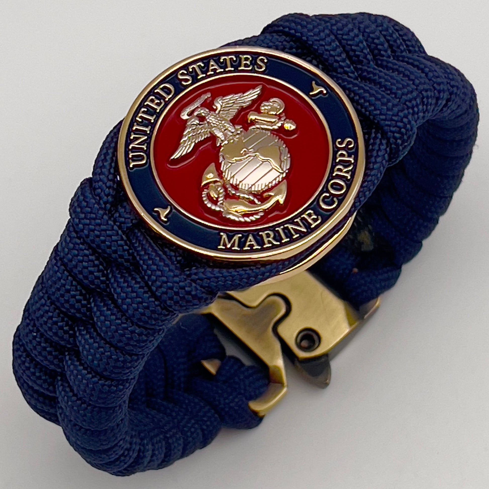 Thick and comfortable braided United States Marine Corps bracelet featuring a 24K gold and silver plated USMC officer Eagle Globe and Anchor medallion, a Cobra style tactical buckle and woven with Navy blue paracord.