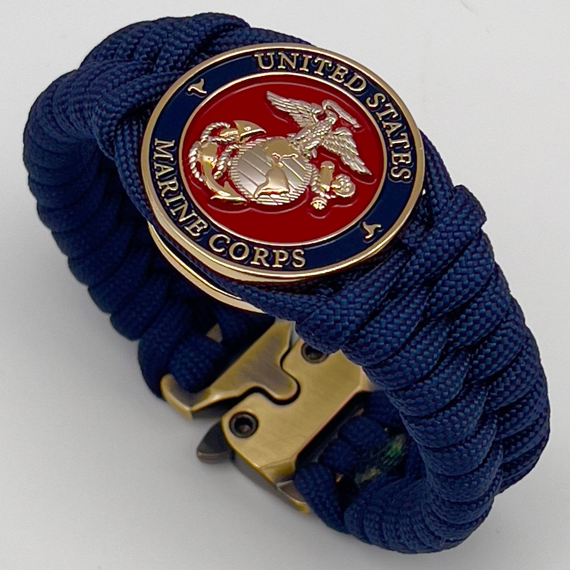Thick and comfortable braided United States Marine Corps bracelet featuring a 24K gold and silver plated USMC officer Eagle Globe and Anchor medallion, a Cobra style tactical buckle and woven with Navy blue paracord.