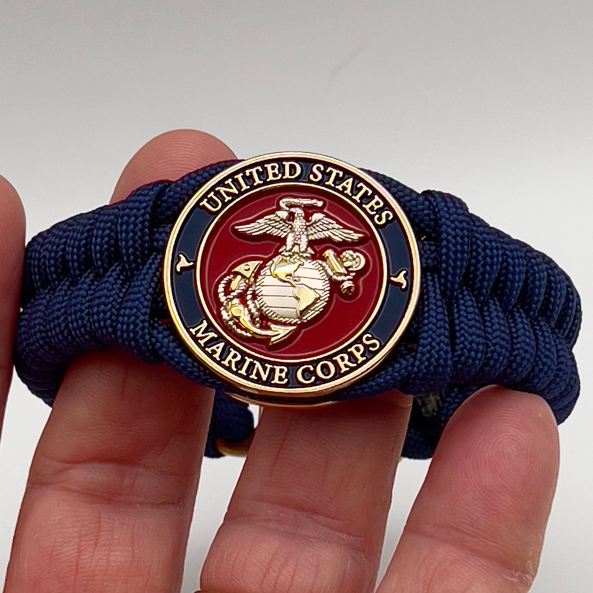 Thick and comfortable braided United States Marine Corps bracelet featuring a 24K gold and silver plated USMC officer Eagle Globe and Anchor medallion, a Cobra style tactical buckle and woven with Navy blue paracord.