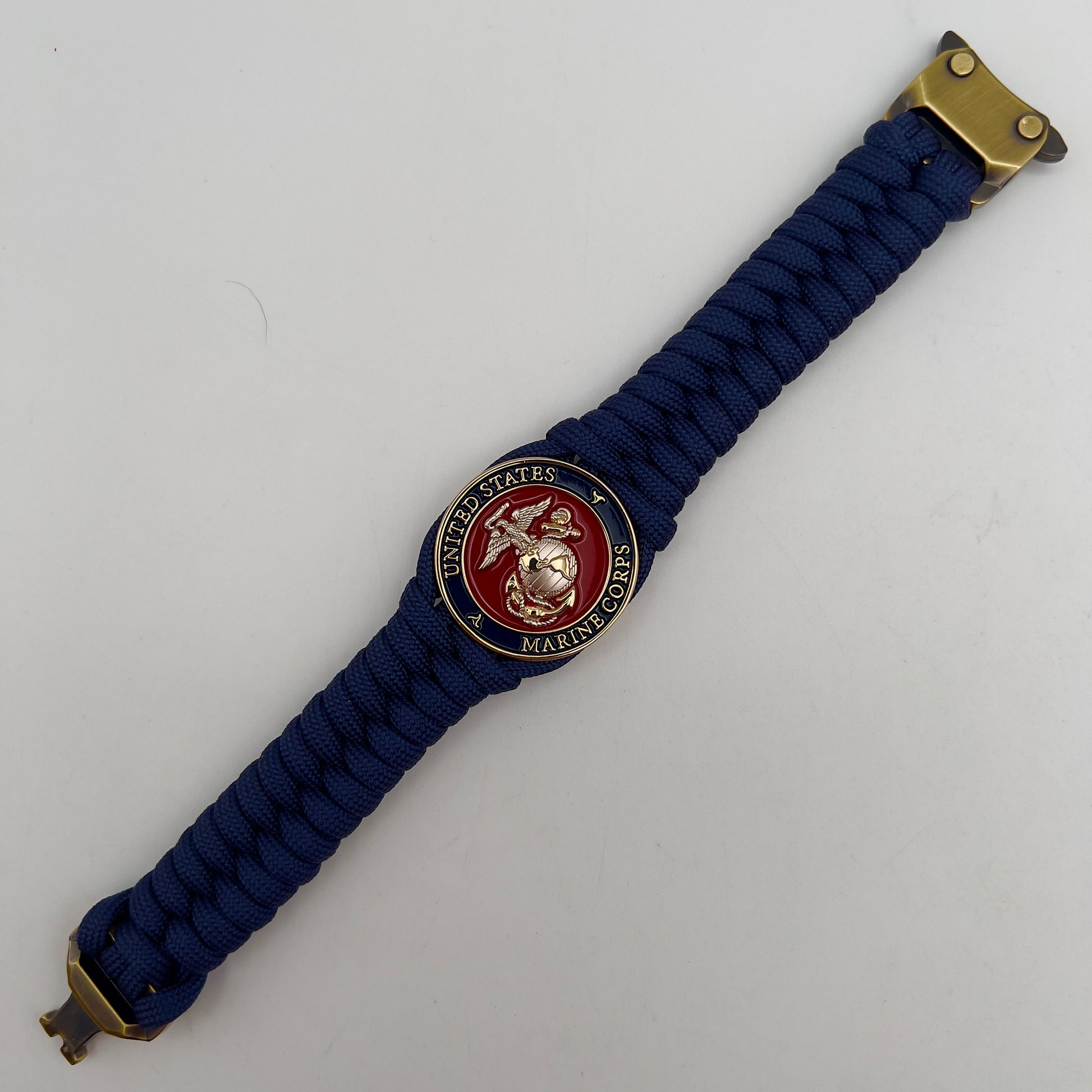 Thick and comfortable braided United States Marine Corps bracelet featuring a 24K gold and silver plated USMC officer Eagle Globe and Anchor medallion, a Cobra style tactical buckle and woven with Navy blue paracord.