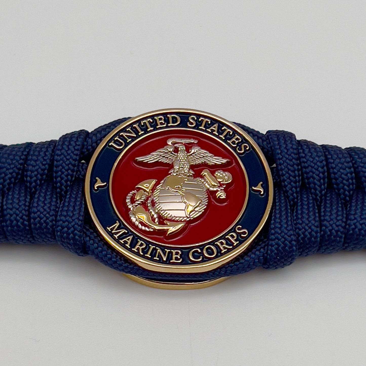 Thick and comfortable braided United States Marine Corps bracelet featuring a 24K gold and silver plated USMC officer Eagle Globe and Anchor medallion, a Cobra style tactical buckle and woven with Navy blue paracord.