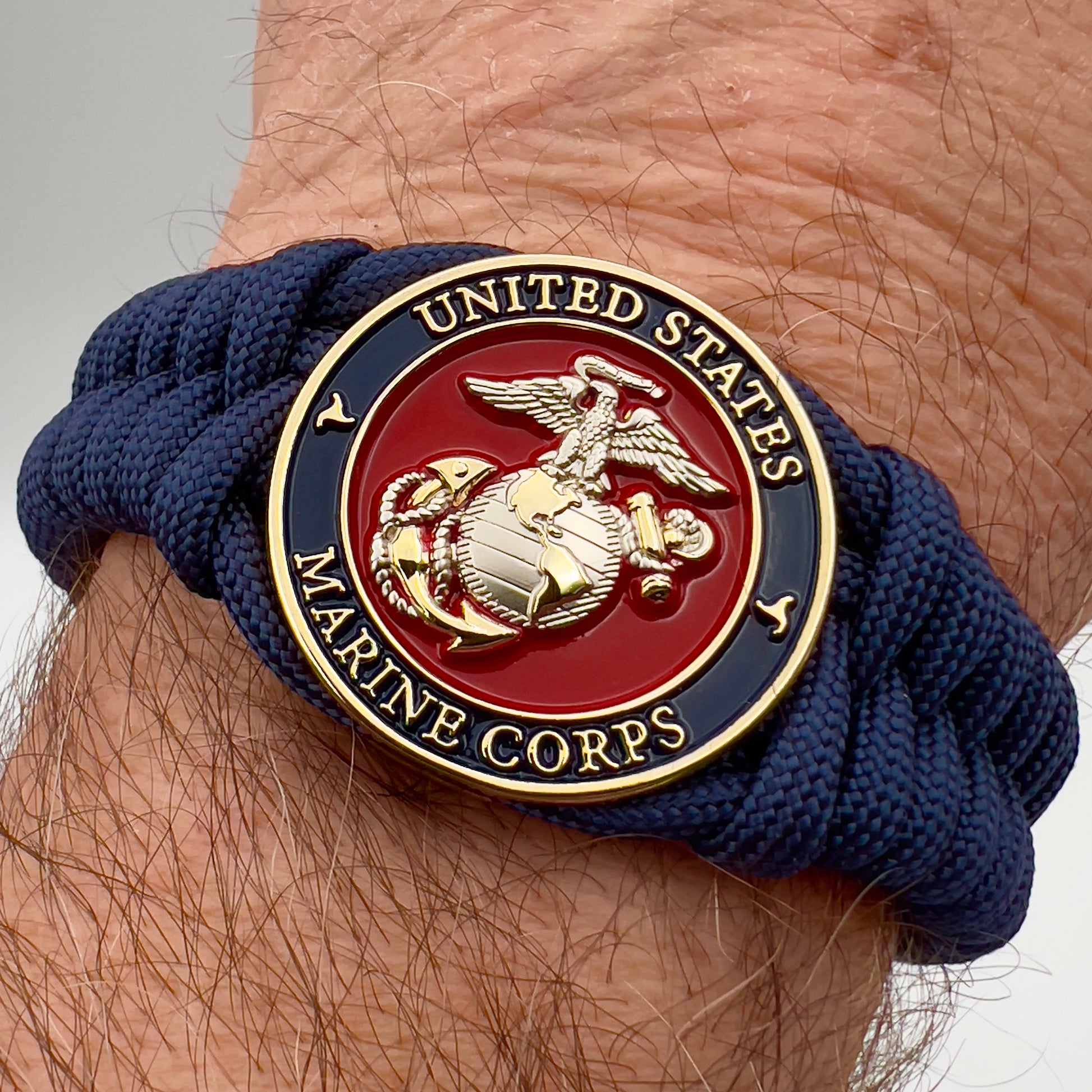 Thick and comfortable braided United States Marine Corps bracelet featuring a 24K gold and silver plated USMC officer Eagle Globe and Anchor medallion, a Cobra style tactical buckle and woven with Navy blue paracord.