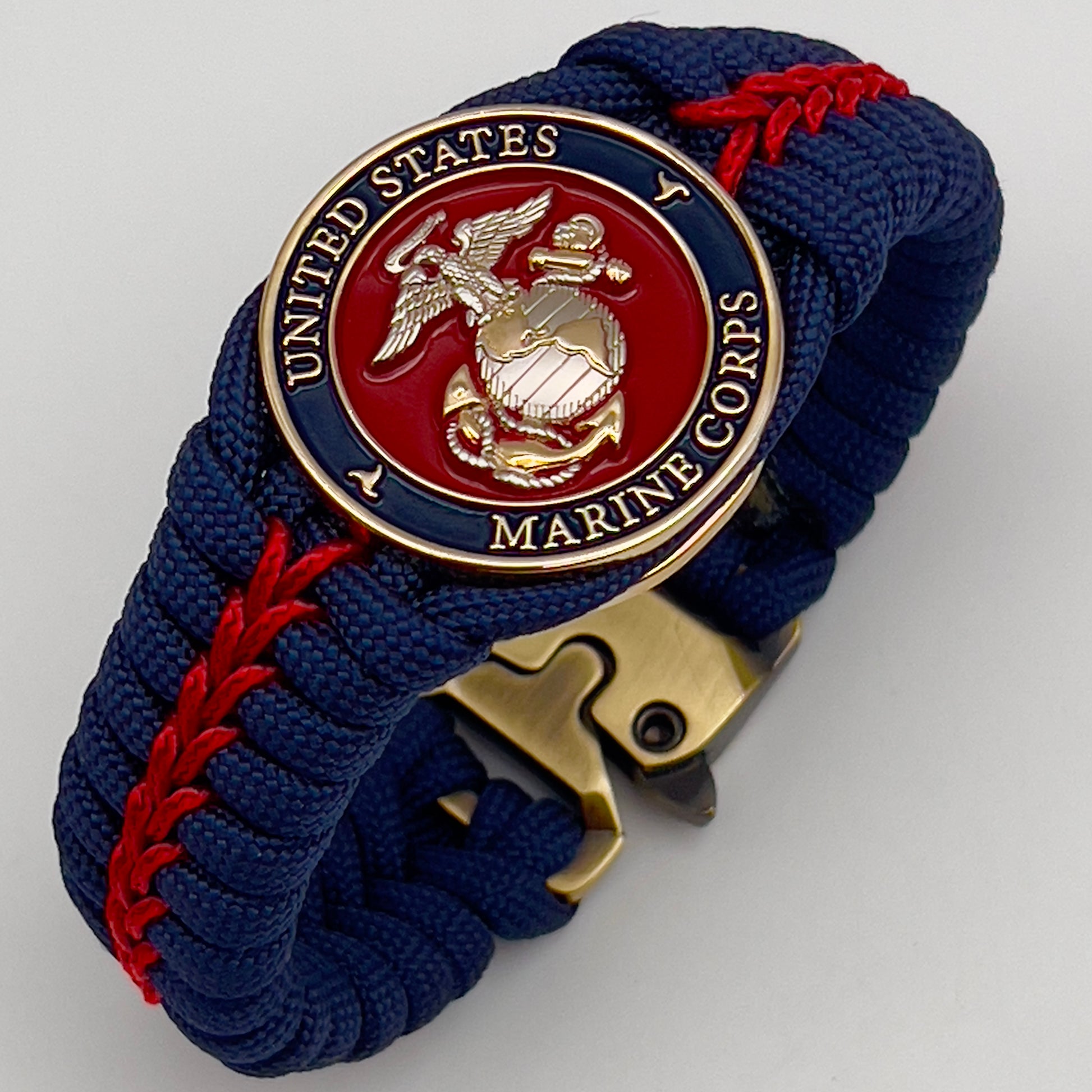 Thick and comfortable braided United States Marine Corps bracelet featuring a 24K gold and silver plated USMC officer Eagle Globe and Anchor medallion, a Cobra style tactical buckle and woven with Navy blue and Imperial red paracord.