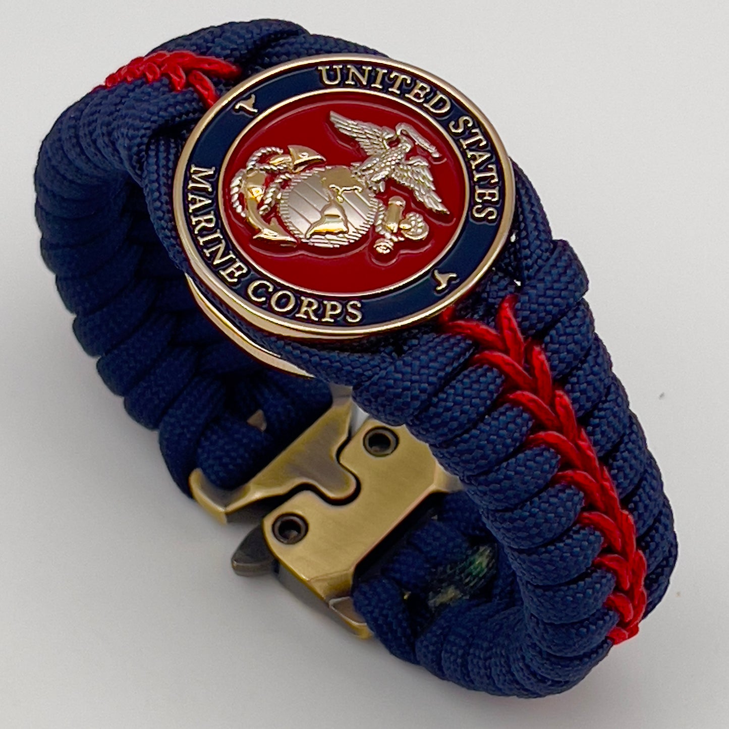Thick and comfortable braided United States Marine Corps bracelet featuring a 24K gold and silver plated USMC officer Eagle Globe and Anchor medallion, a Cobra style tactical buckle and woven with Navy blue and Imperial red paracord.