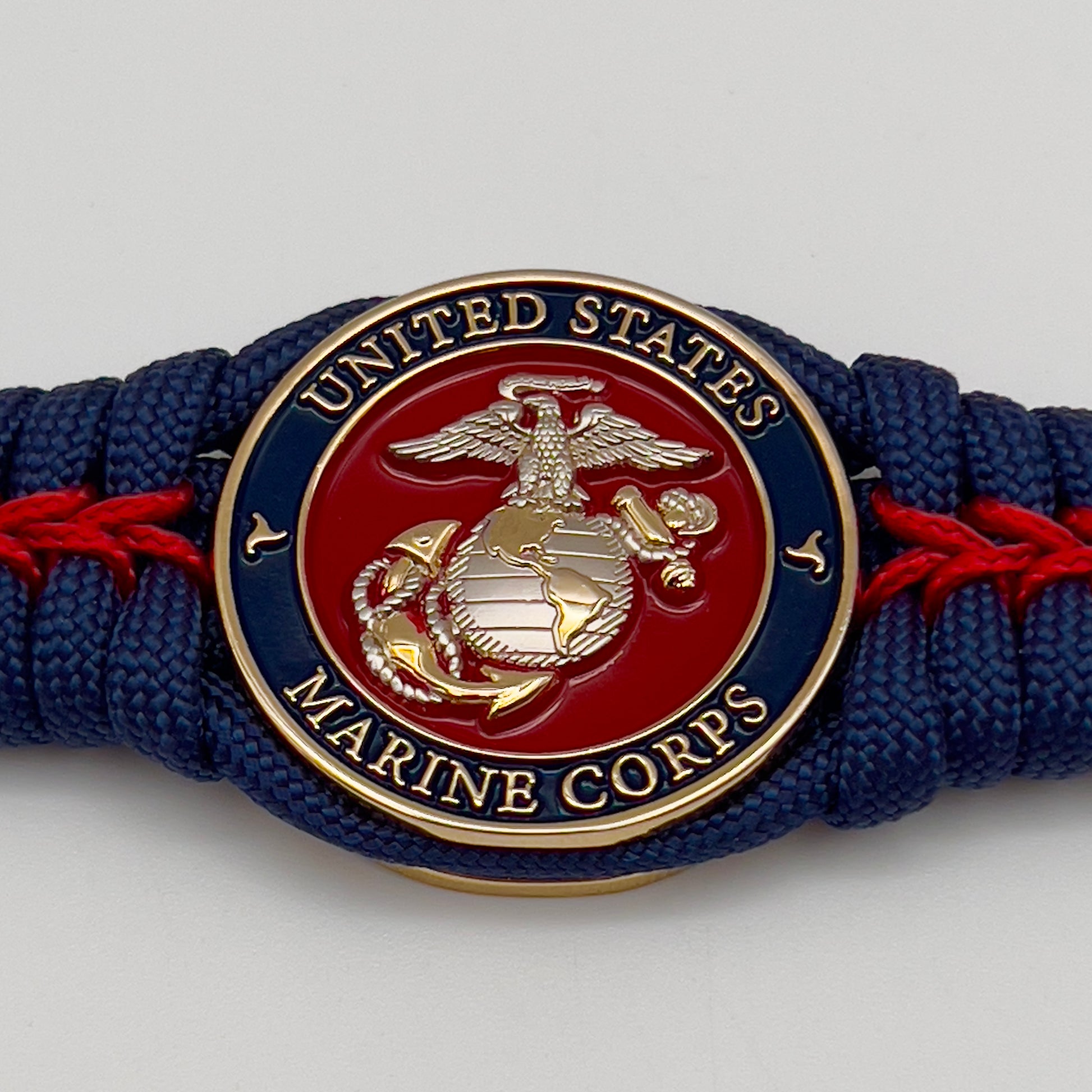 Thick and comfortable braided United States Marine Corps bracelet featuring a 24K gold and silver plated USMC officer Eagle Globe and Anchor medallion, a Cobra style tactical buckle and woven with Navy blue and Imperial red paracord.