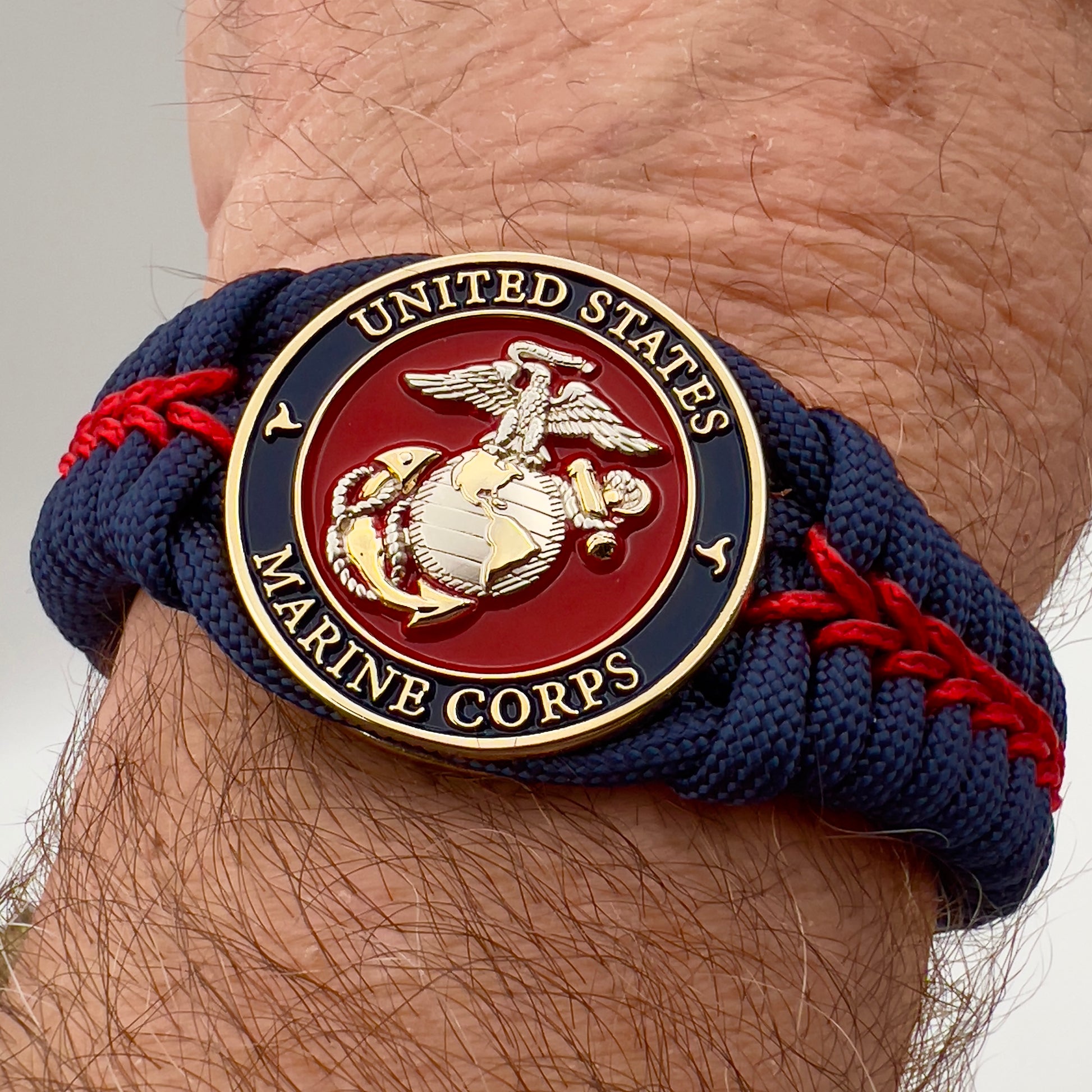 Thick and comfortable braided United States Marine Corps bracelet featuring a 24K gold and silver plated USMC officer Eagle Globe and Anchor medallion, a Cobra style tactical buckle and woven with Navy blue and Imperial red paracord.