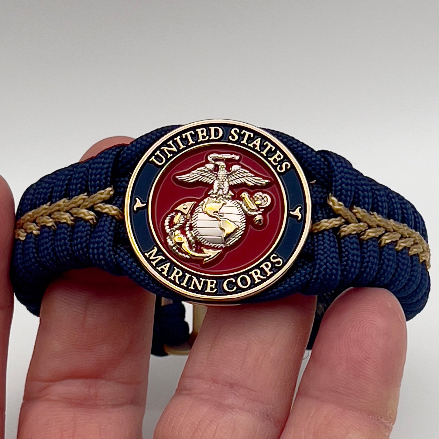 Thick and comfortable braided United States Marine Corps bracelet featuring a 24K gold and silver plated USMC officer Eagle Globe and Anchor medallion, a Cobra style tactical buckle and woven with Navy blue and gold paracord.