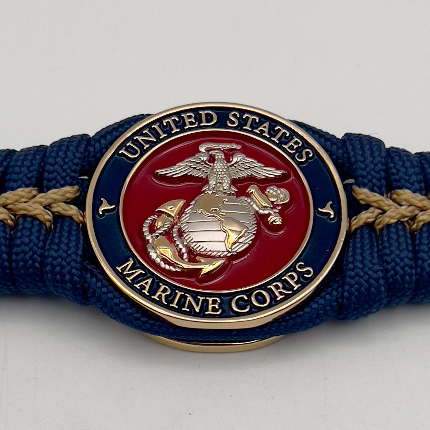 Thick and comfortable braided United States Marine Corps bracelet featuring a 24K gold and silver plated USMC officer Eagle Globe and Anchor medallion, a Cobra style tactical buckle and woven with Navy blue and gold paracord.