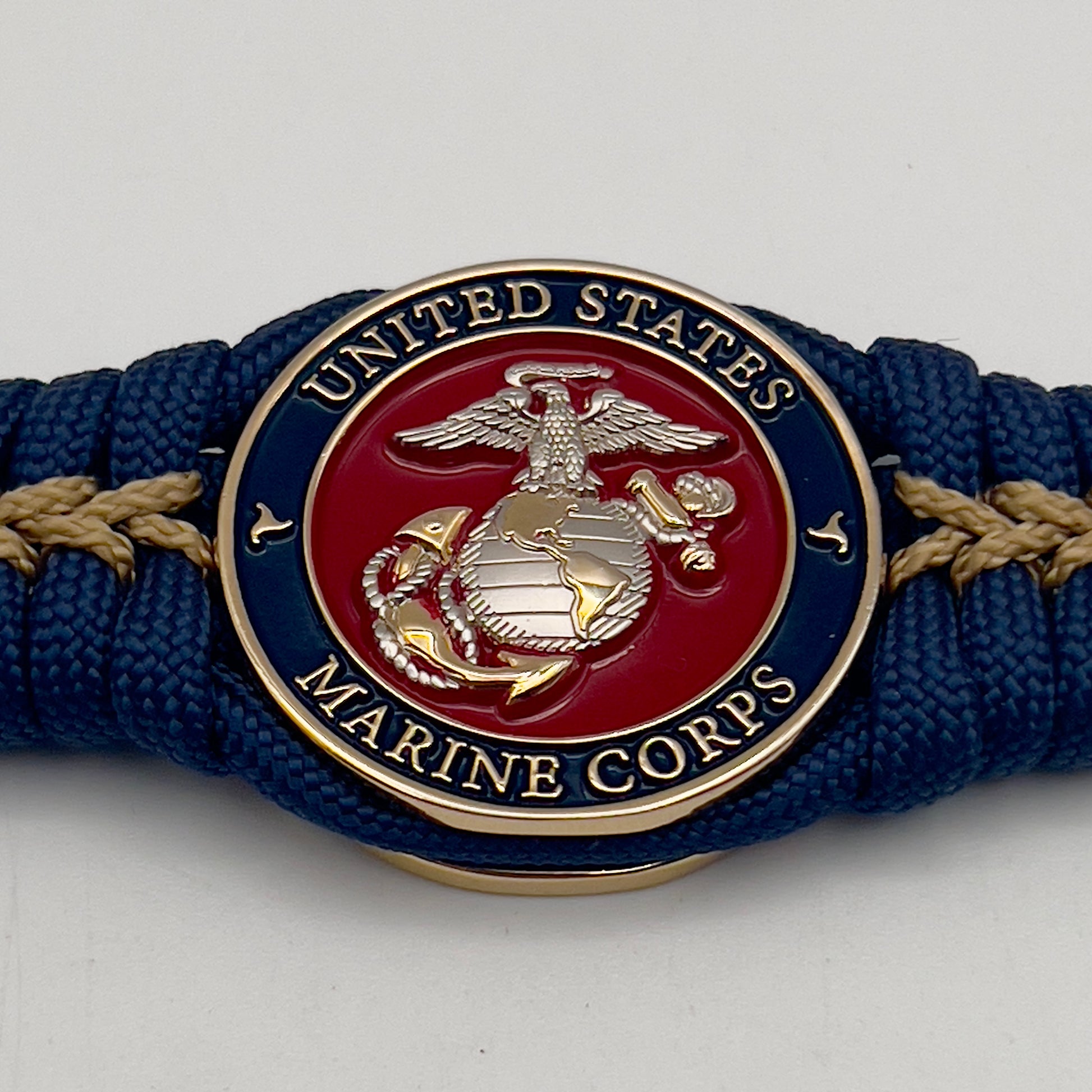 Thick and comfortable braided United States Marine Corps bracelet featuring a 24K gold and silver plated USMC officer Eagle Globe and Anchor medallion, a Cobra style tactical buckle and woven with Navy blue and gold paracord.