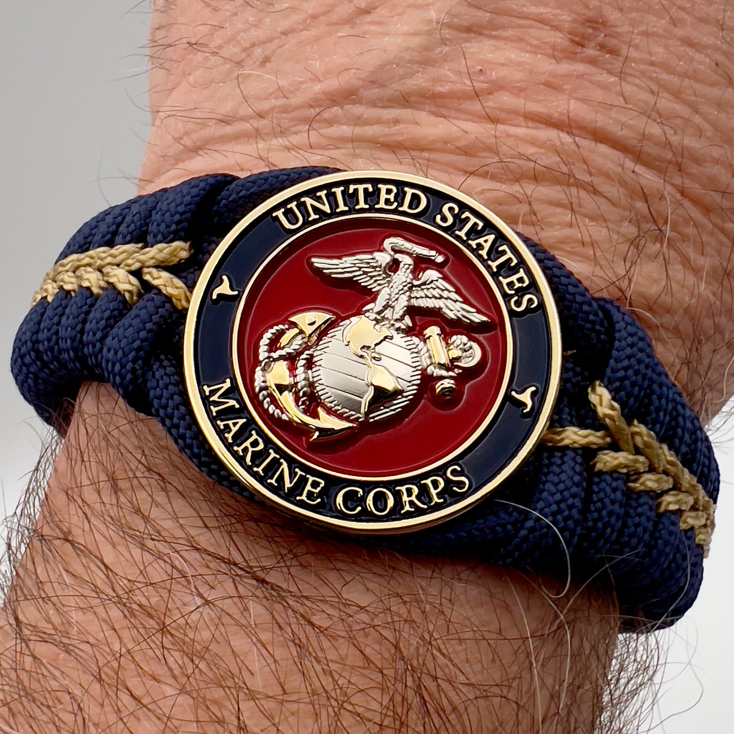 Thick and comfortable braided United States Marine Corps bracelet featuring a 24K gold and silver plated USMC officer Eagle Globe and Anchor medallion, a Cobra style tactical buckle and woven with Navy blue and gold paracord.