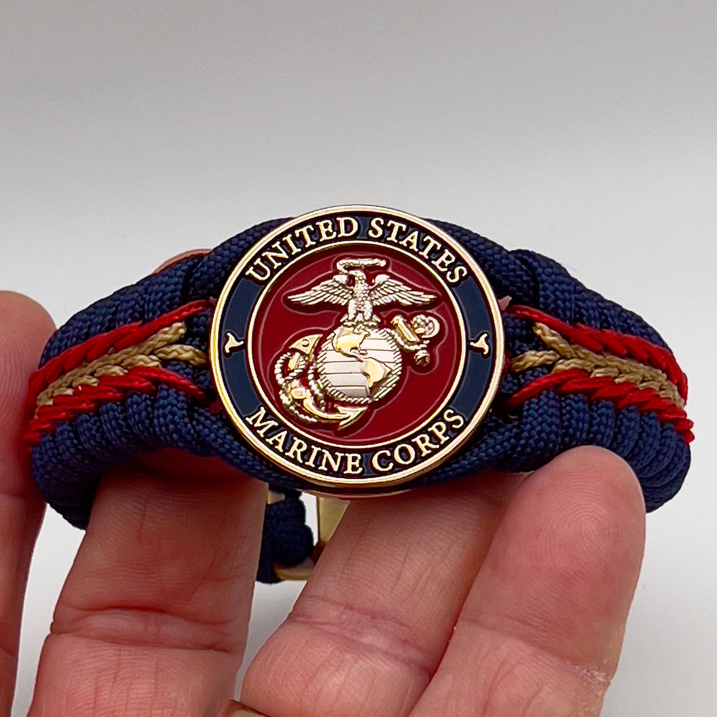 Thick and comfortable braided United States Marine Corps bracelet featuring a 24K gold and silver plated USMC officer Eagle Globe and Anchor medallion, a Cobra style tactical buckle and woven with Navy blue, Imperial red and gold paracord.