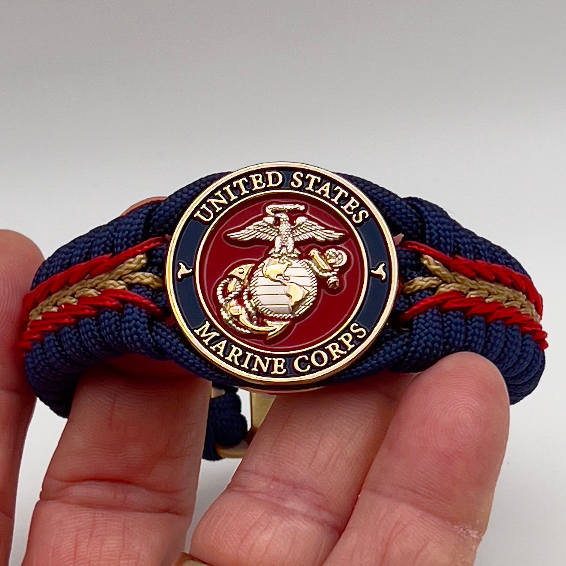 Thick and comfortable braided United States Marine Corps bracelet featuring a 24K gold and silver plated USMC officer Eagle Globe and Anchor medallion, a Cobra style tactical buckle and woven with Navy blue, Imperial red and gold paracord.